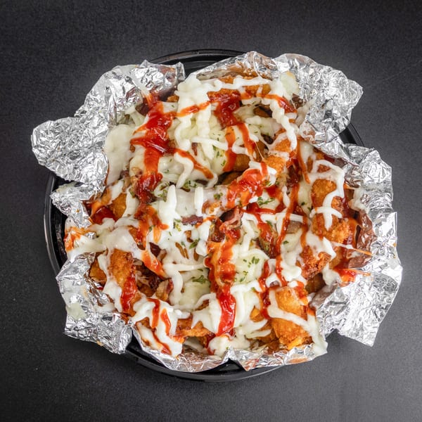 Loaded tater tots with melted cheese, ketchup, and mayonnaise in a foil-lined container.