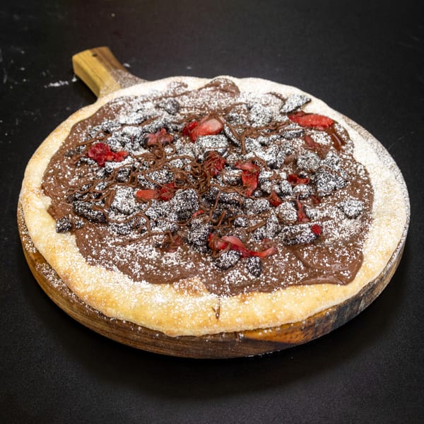 Dessert pizza with chocolate spread, strawberries, chocolate shavings, and powdered sugar on a wooden board.
