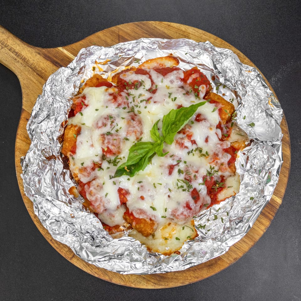 Chicken parmesan with melted mozzarella, tomato sauce, and basil on a wooden board.