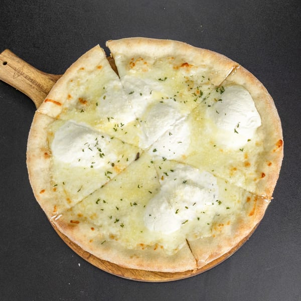 A white pizza with dollops of ricotta cheese and parsley, sliced on a wooden board.