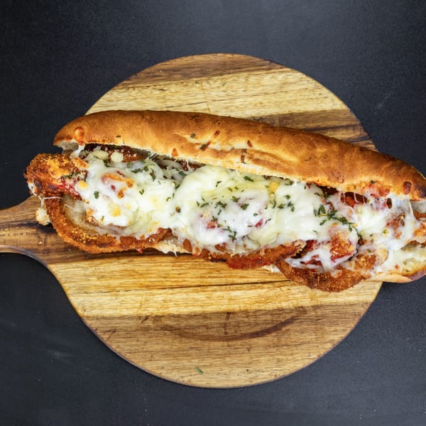 A chicken parmesan hero sandwich, overflowing with melted mozzarella cheese and red sauce, on a wooden board.