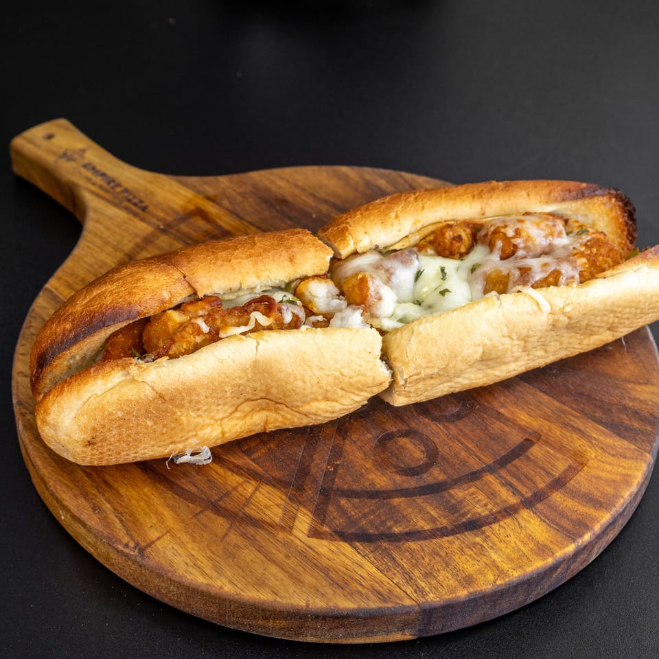 A chicken parmesan hero sandwich, cut in half, on a wooden serving board.