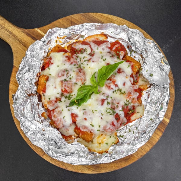Chicken parmesan with melted mozzarella, red sauce, and basil on a wooden board with foil.
