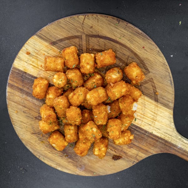 Golden-brown tater tots, sprinkled with herbs, piled on a rustic wooden serving board.