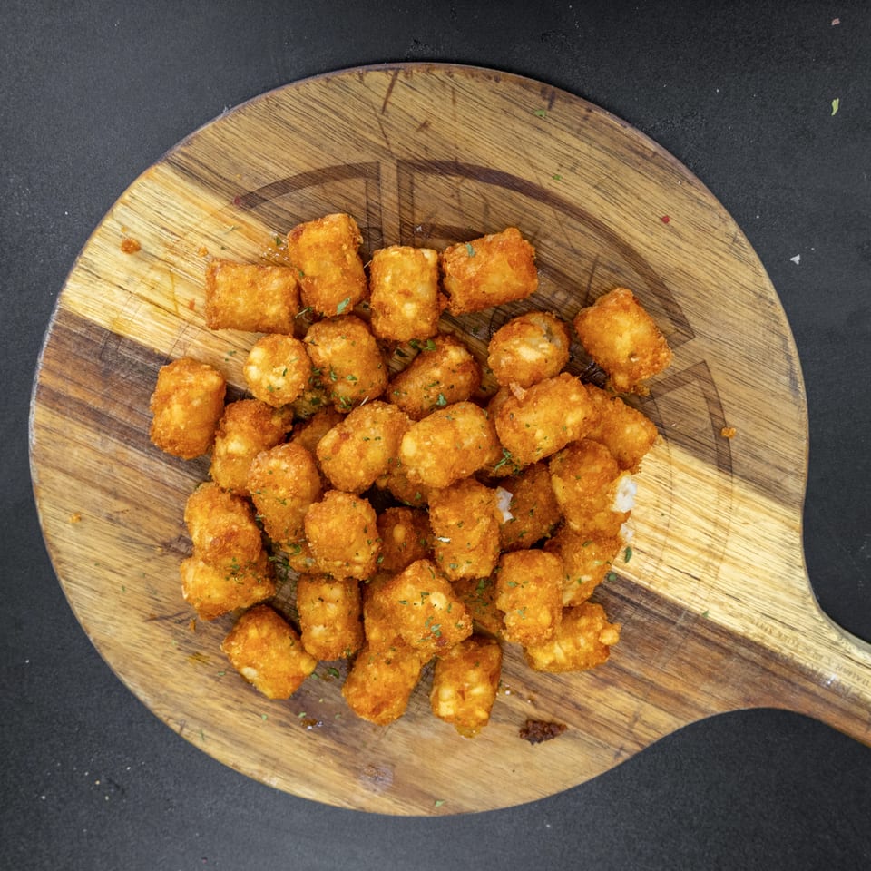 Crispy golden fried bites sprinkled with herbs, piled on a rustic wooden serving board against a dark background.